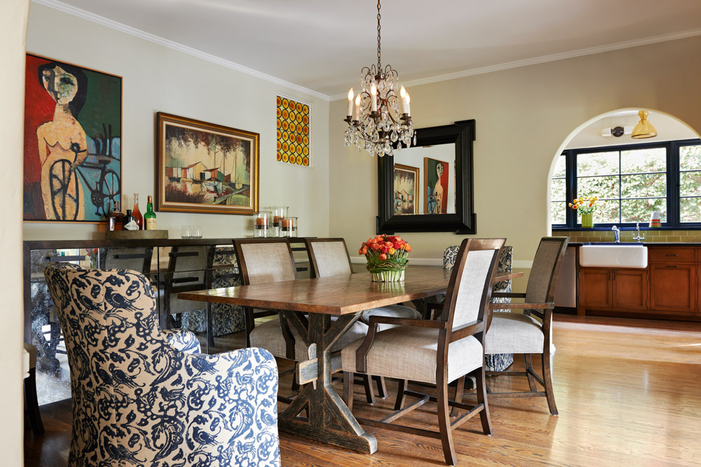 A warm and eclectic dining room features patterned side chairs that bring in an extra layer of texture. The walls exhibit vintage art, a map of London and a dark wood framed mirror.